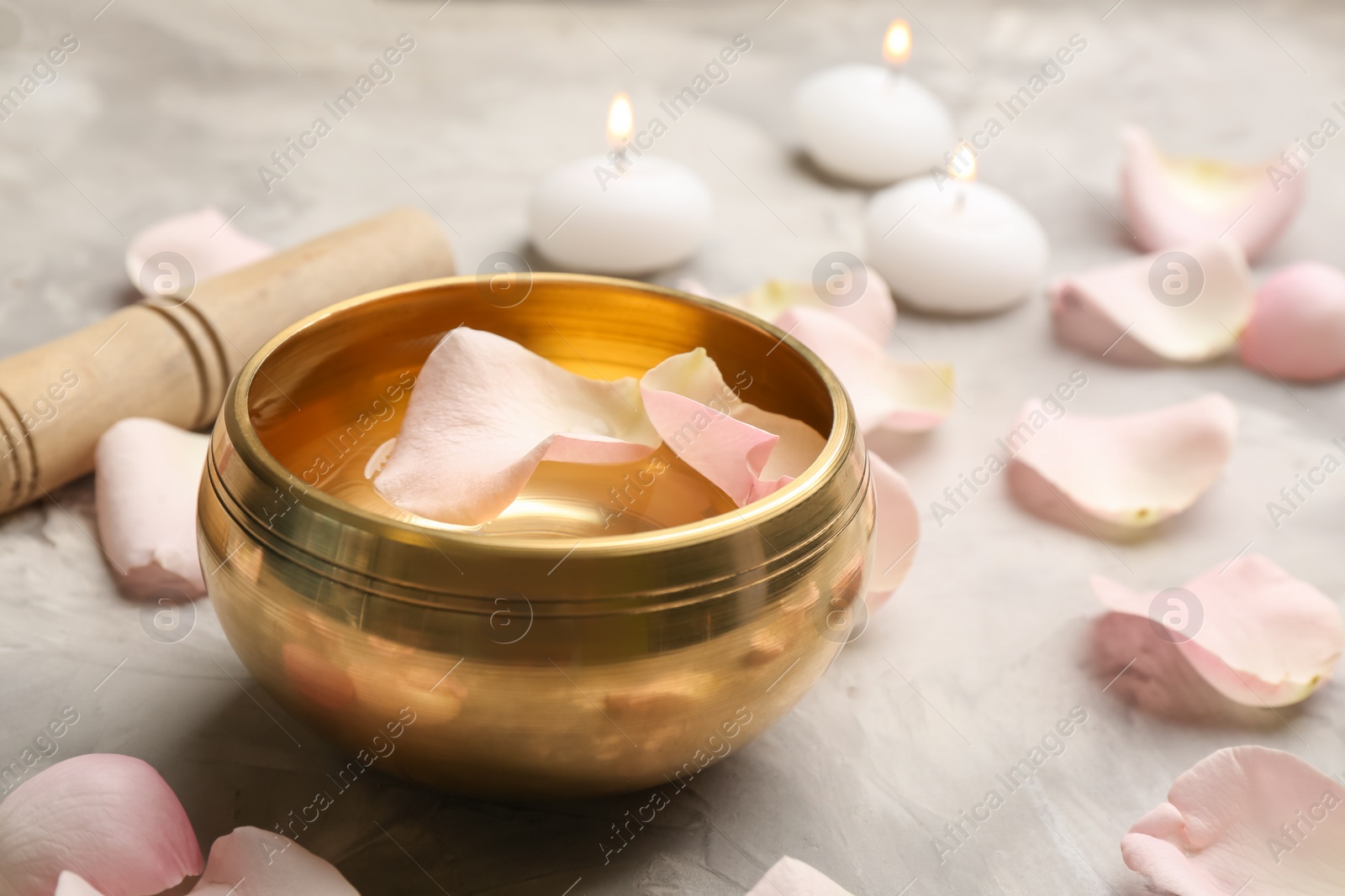Photo of Golden singing bowl with petals and mallet on grey table, closeup. Sound healing