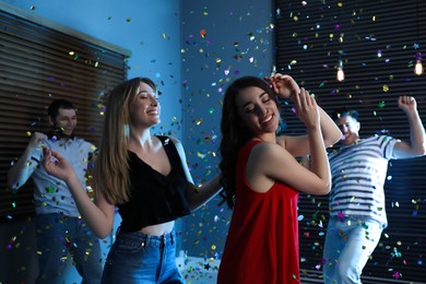 Photo of Happy friends and falling confetti in dark room