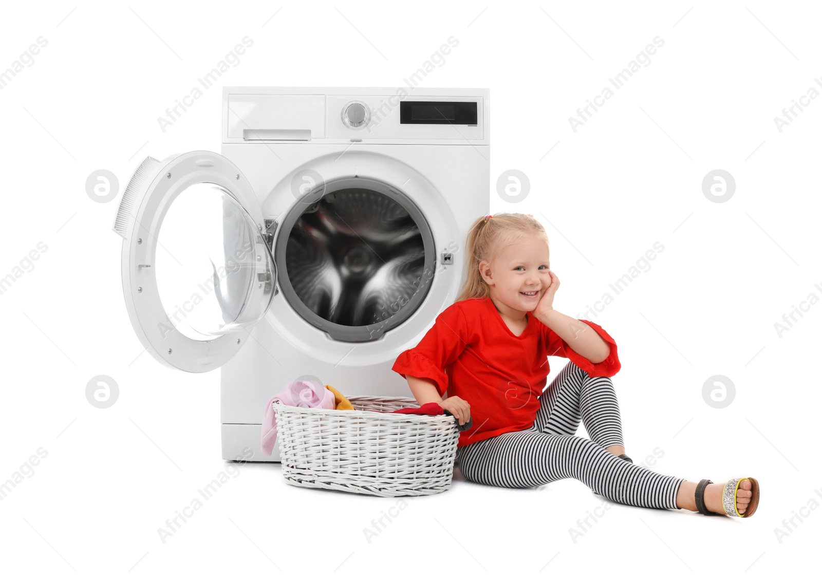 Photo of Cute little girl sitting near basket with laundry and washing machine on white background