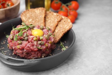 Photo of Tasty beef steak tartare served with yolk, capers and bread on light grey table. Space for text