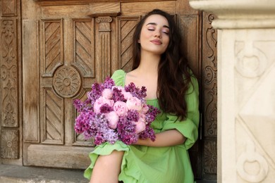 Beautiful woman with bouquet of spring flowers near building outdoors