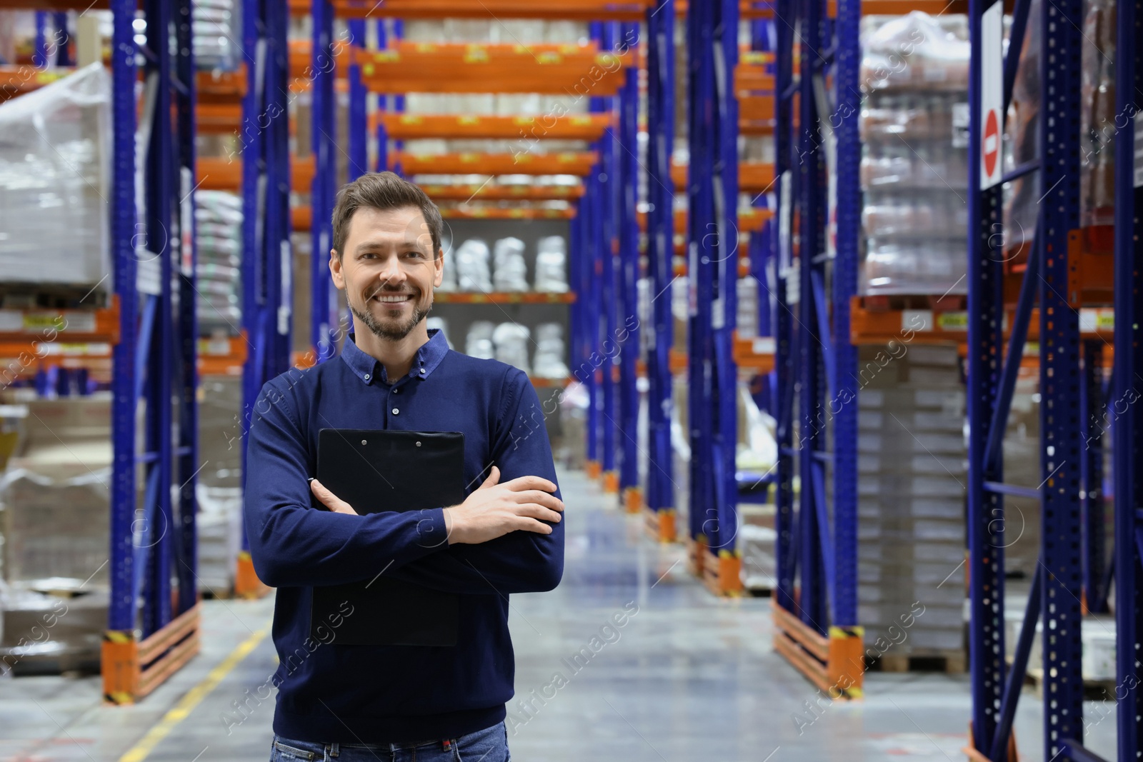 Photo of Happy manager holding clipboard in warehouse with lots of products. Space for text