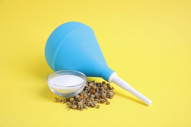 Photo of Blue enema, soda powder and dry chamomile flowers on yellow background