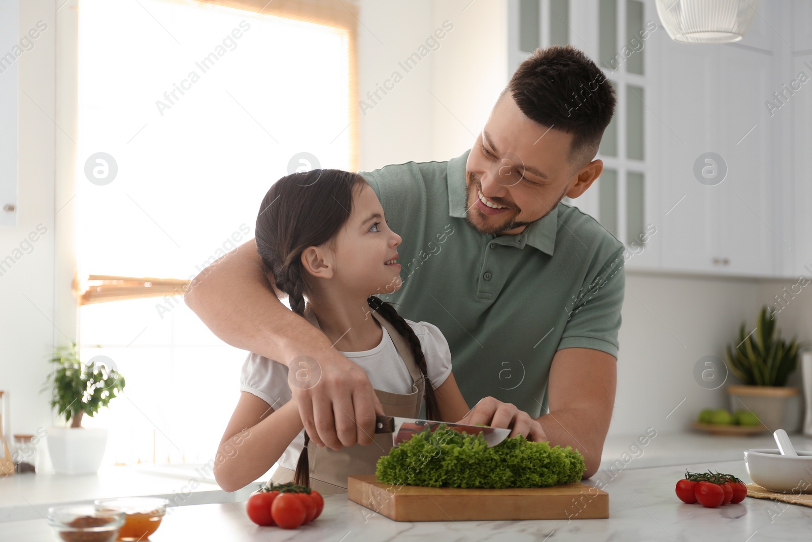 Photo of Father and daughter cutting lettuce in kitchen. Cooking together
