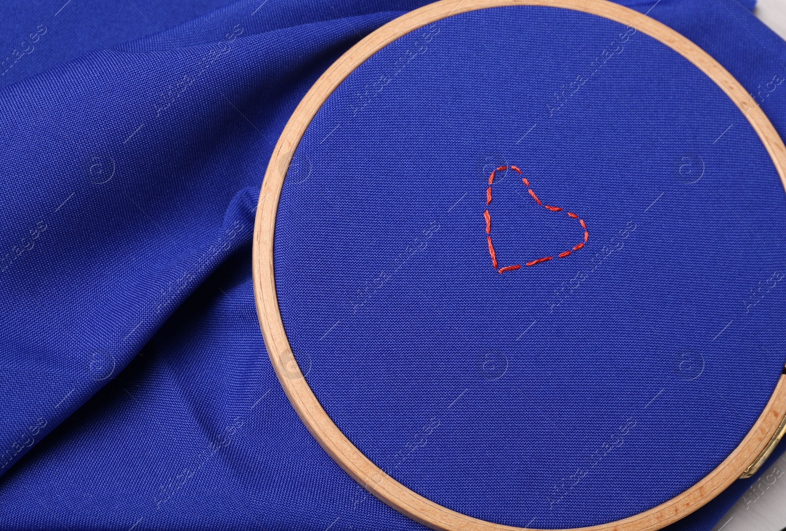 Photo of Red embroidered heart on blue cloth with hoop, top view