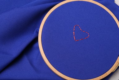 Red embroidered heart on blue cloth with hoop, top view