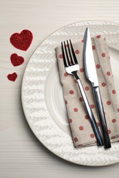 Photo of Plate with cutlery and decorative hearts on white wooden table for romantic dinner, top view