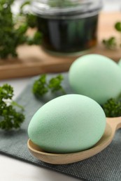 Photo of Turquoise Easter eggs painted with natural dye and curly parsley on table, closeup