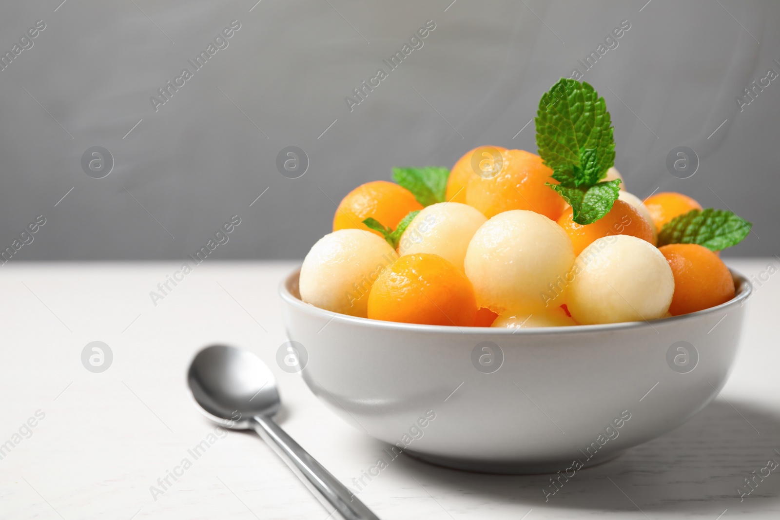 Photo of Melon balls and mint in bowl on white wooden table, closeup
