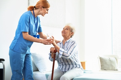 Photo of Nurse giving glass of water to elderly woman indoors. Medical assistance