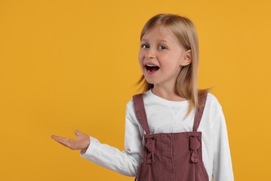 Photo of Special promotion. Little girl showing something on orange background. Space for text