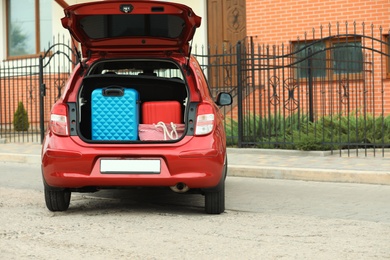 Photo of Suitcases and tote bag in car trunk on city street. Space for text