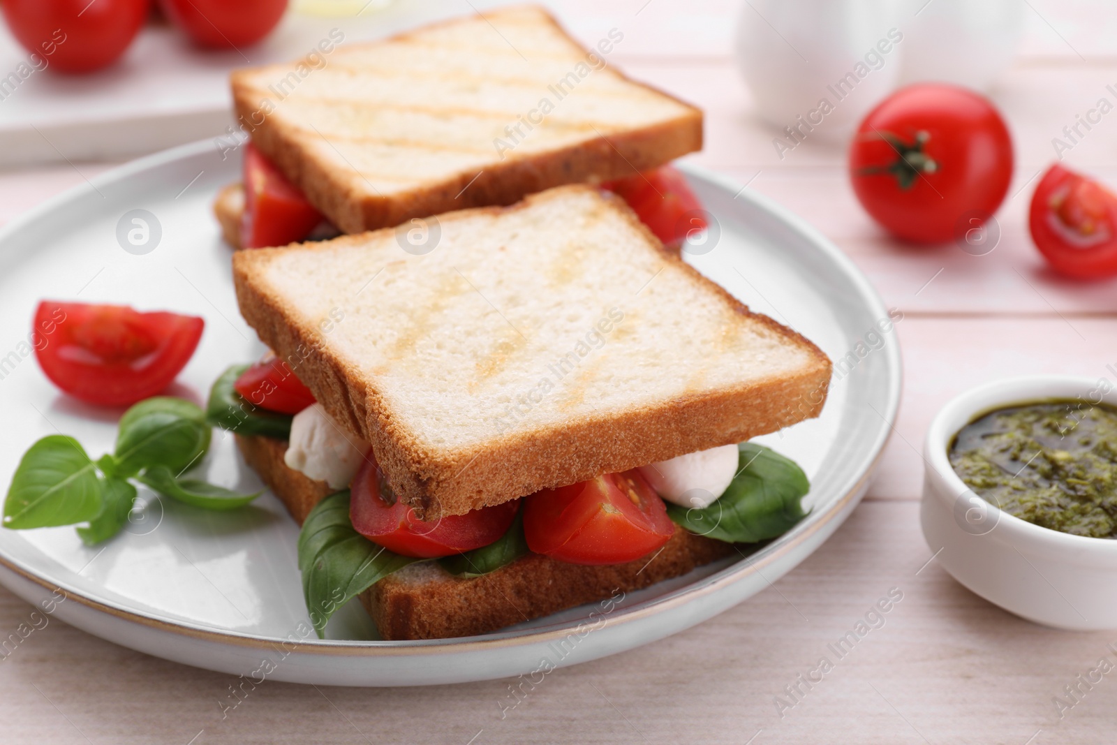 Photo of Delicious Caprese sandwiches with mozzarella, tomatoes, basil and pesto sauce on white wooden table, closeup