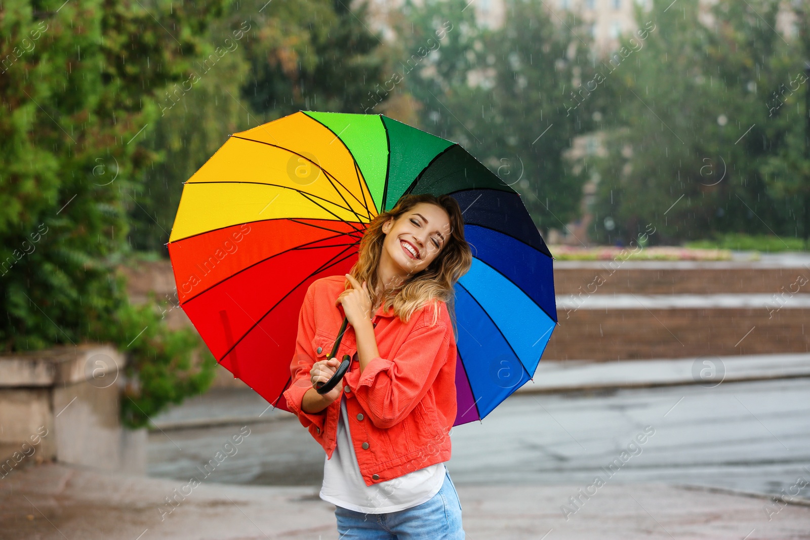 Photo of Happy young woman with bright umbrella under rain outdoors