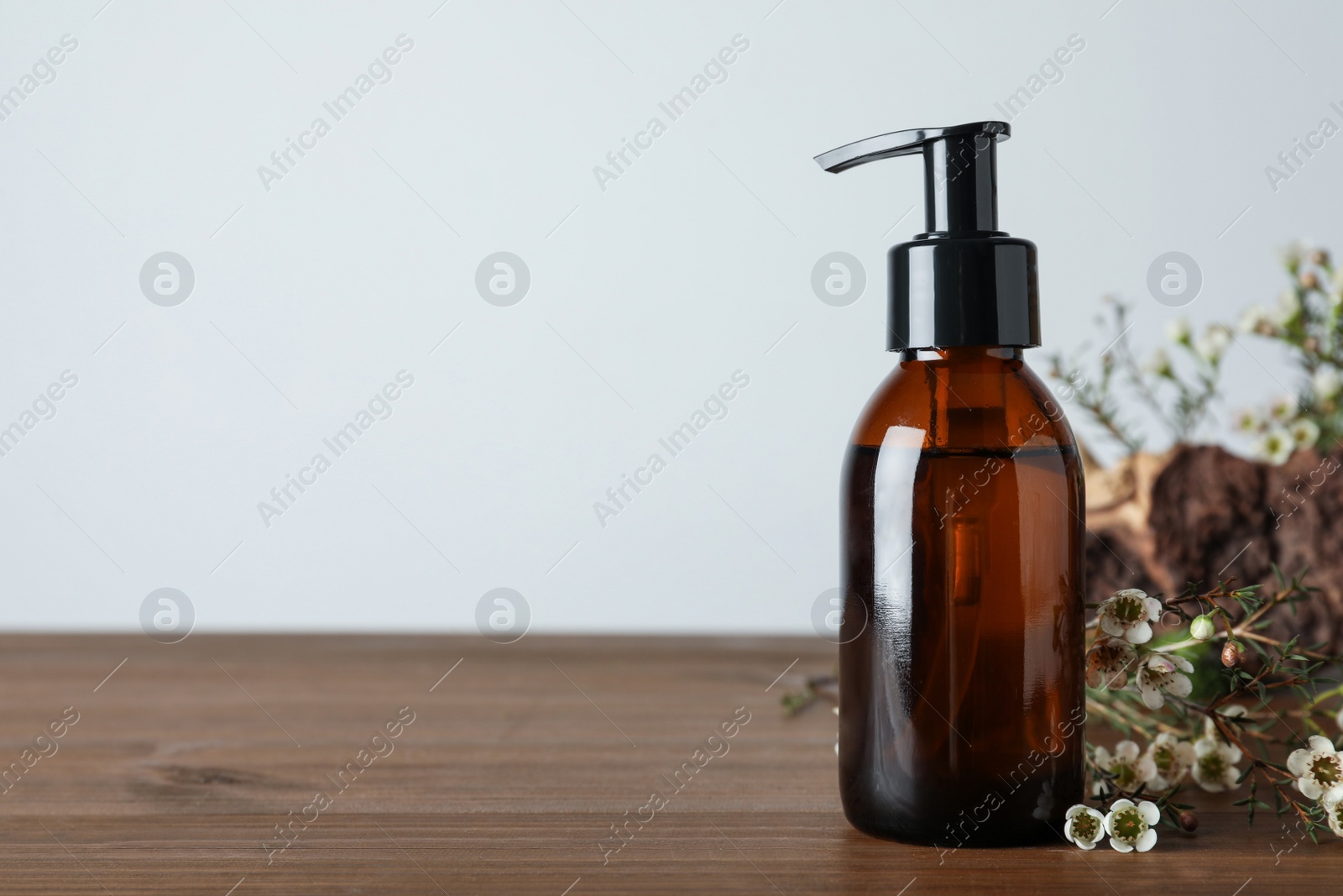 Photo of Bottle of hydrophilic oil and beautiful flowers on wooden table, space for text