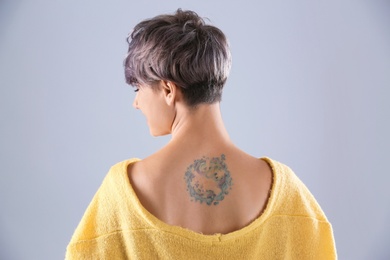 Young woman with tattoo on color background