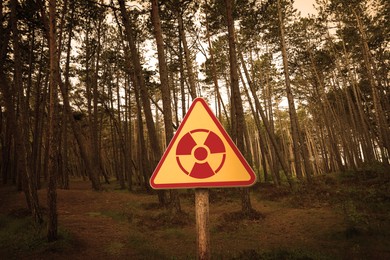 Image of Radioactive pollution. Yellow warning sign with hazard symbol near contaminated area in forest