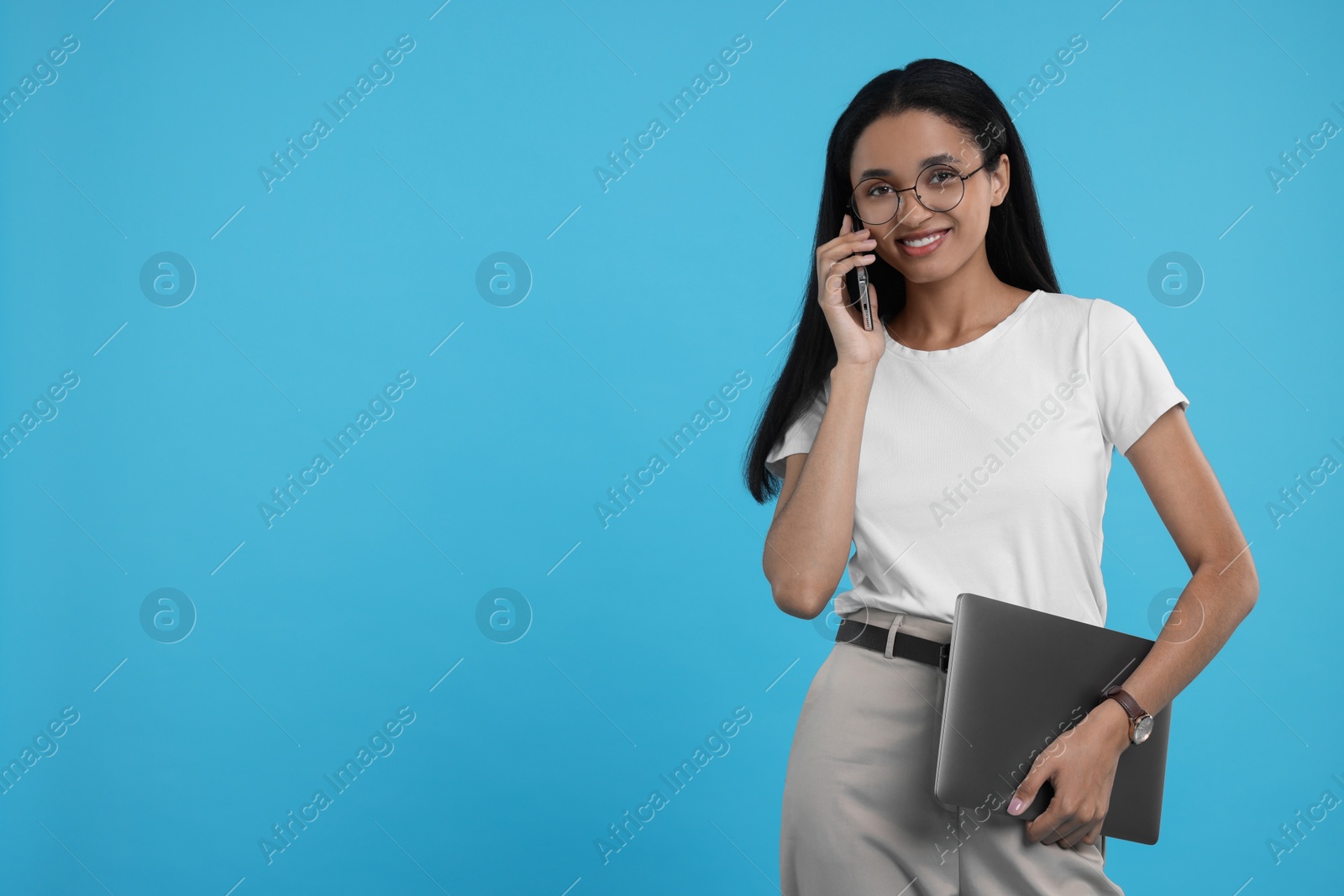Photo of Beautiful secretary with laptop talking on phone against light blue background, space for text