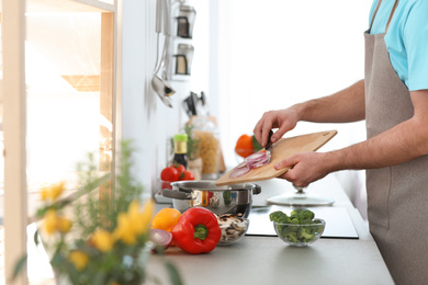 Young man cooking delicious vegetable soup in kitchen, closeup