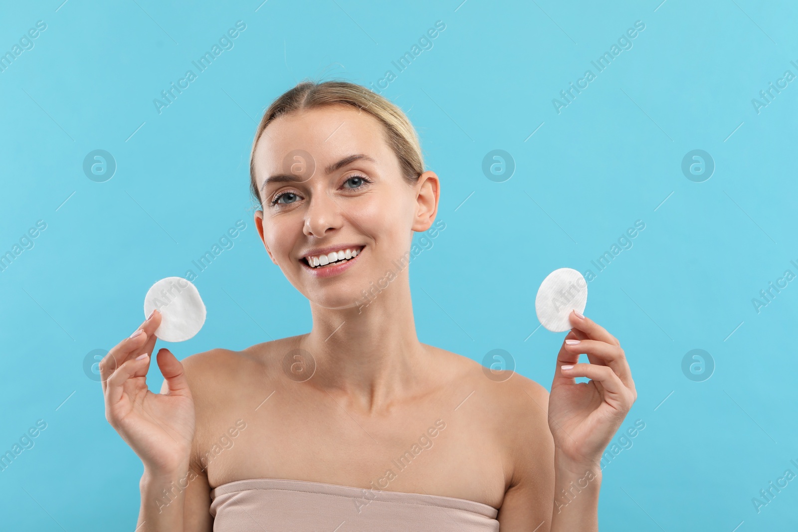 Photo of Removing makeup. Smiling woman with cotton pads on light blue background