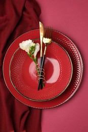 Stylish table setting with cutlery and floral decor on pink background, top view