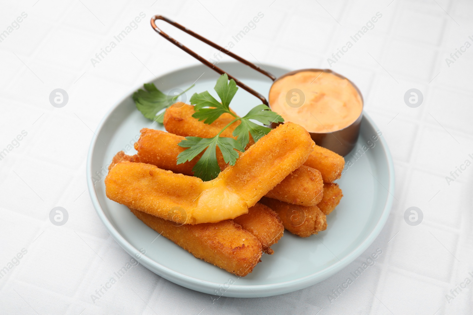 Photo of Tasty fried mozzarella sticks served with sauce and parsley on white tiled table