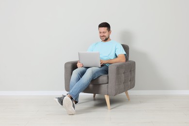 Photo of Happy man sitting in armchair and using laptop indoors