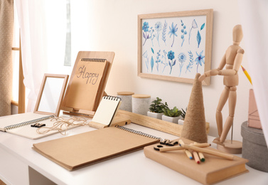 Photo of Wooden human figure and stationery on white table indoors. Interior elements