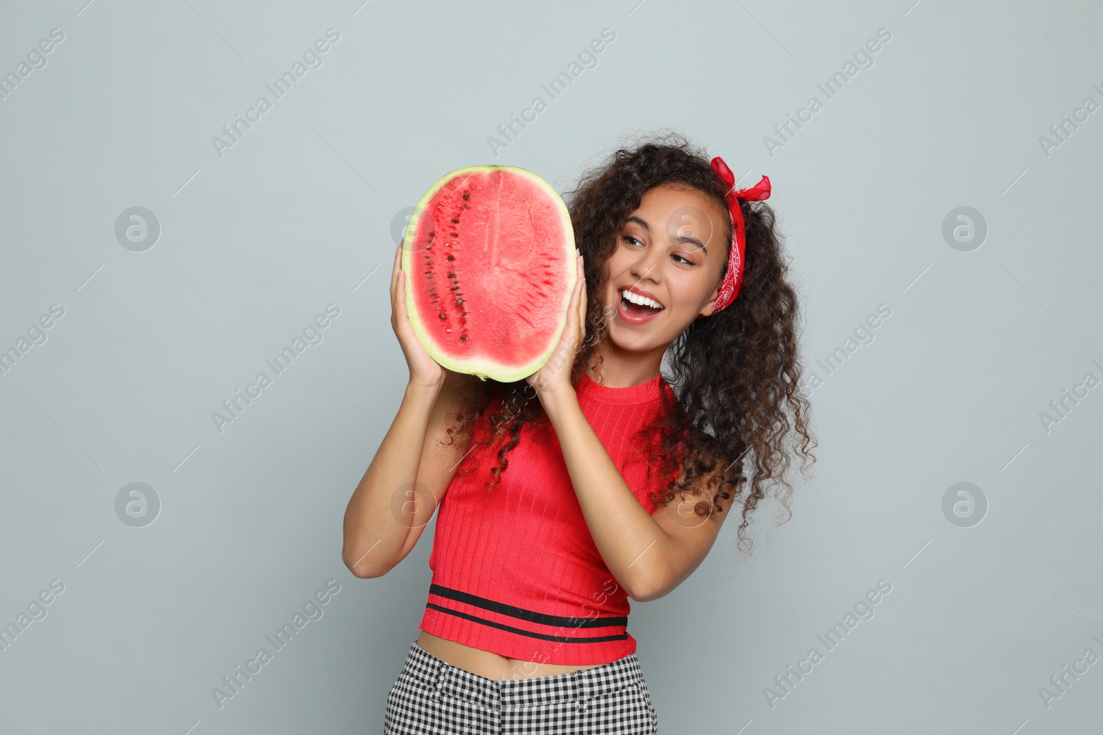 Photo of Beautiful young African American woman with half of watermelon on grey background