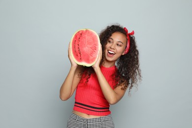 Beautiful young African American woman with half of watermelon on grey background