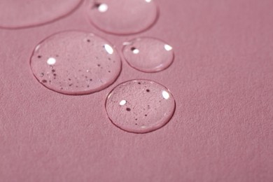 Drops of cosmetic serum on pink background, closeup. Space for text