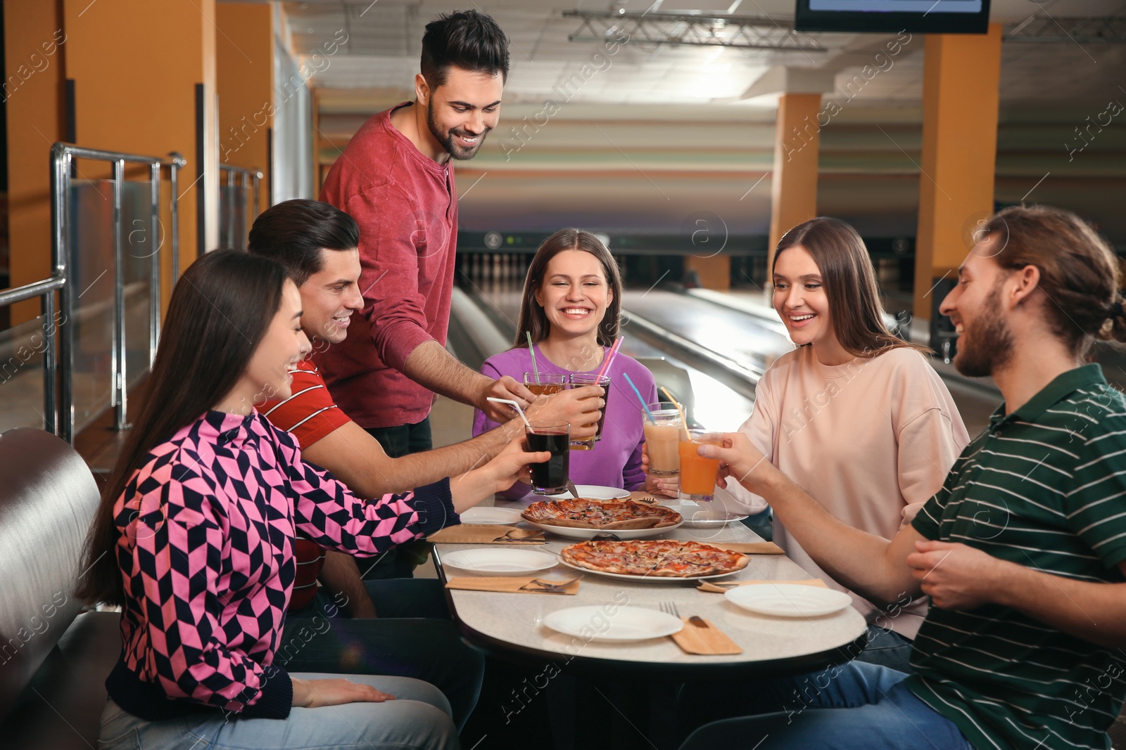 Photo of Group of friends with drinks and pizza in bowling club