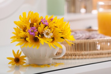 Beautiful bright flowers in cup on white table. Space for text