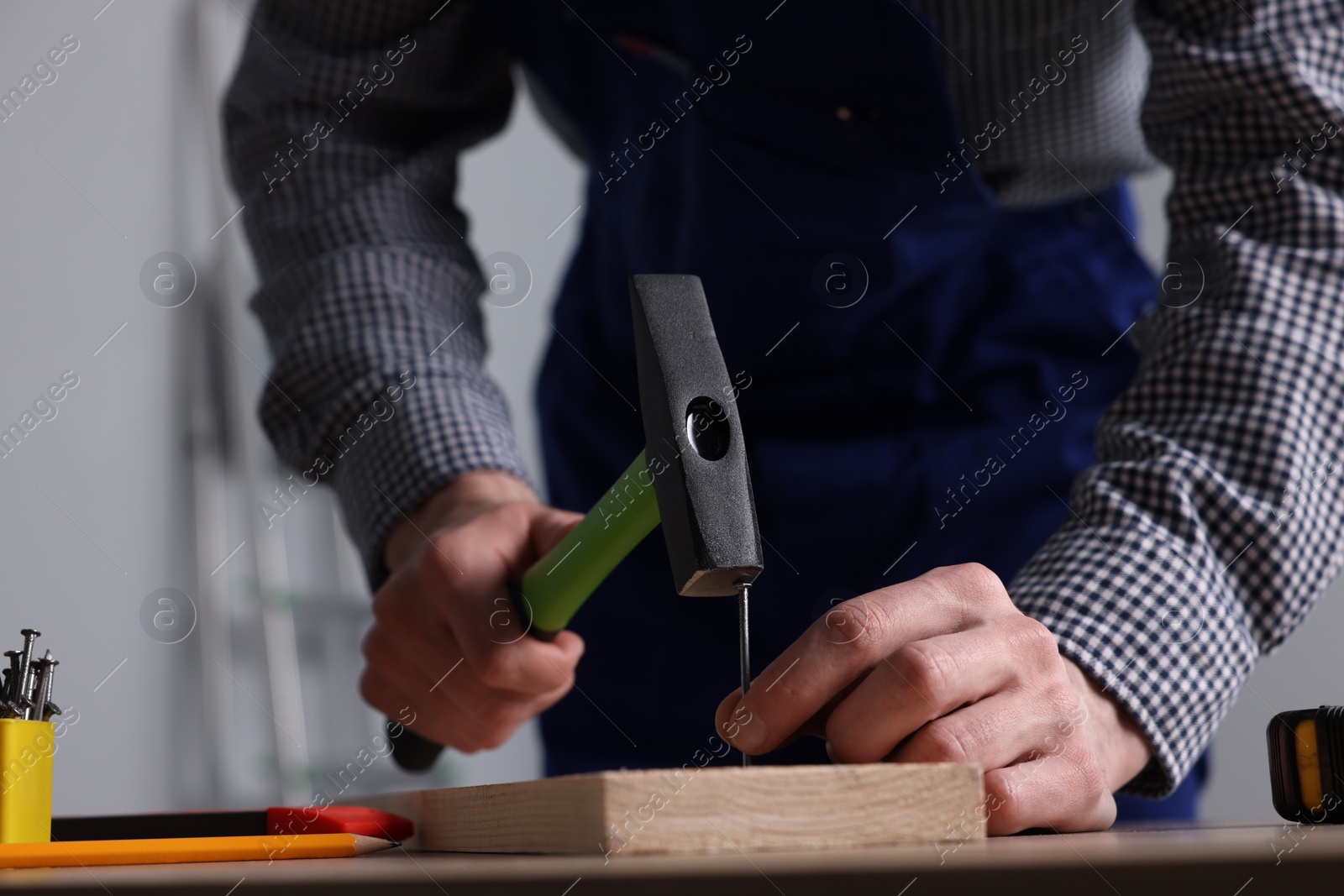 Photo of Professional repairman hammering nail into board at wooden table indoors, closeup