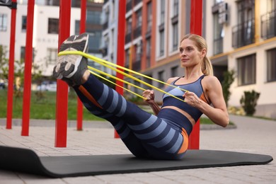 Photo of Athletic woman doing exercise with fitness elastic band on mat at outdoor gym