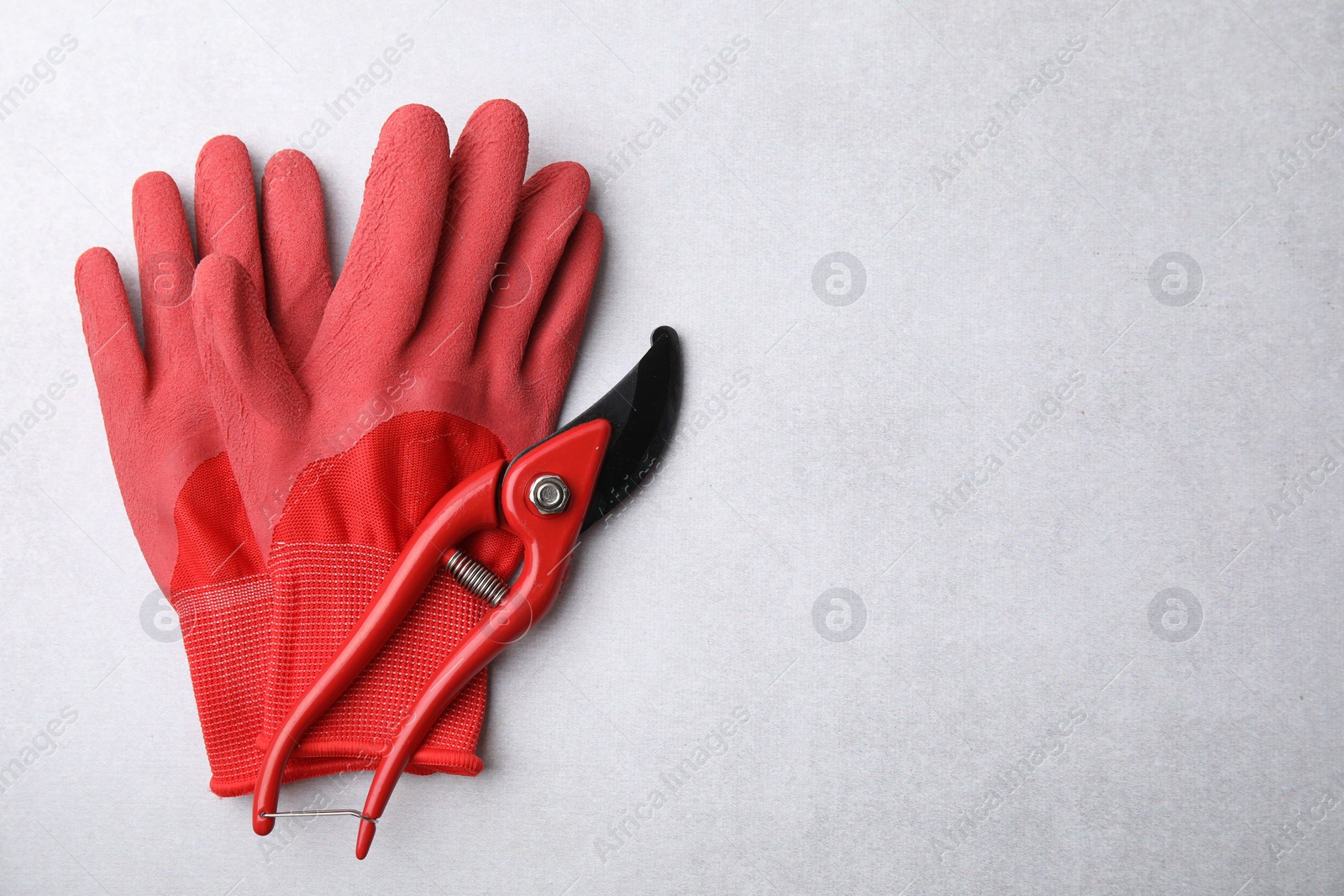Photo of Pair of red gardening gloves and secateurs on light grey table, top view. Space for text