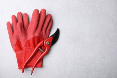 Pair of red gardening gloves and secateurs on light grey table, top view. Space for text