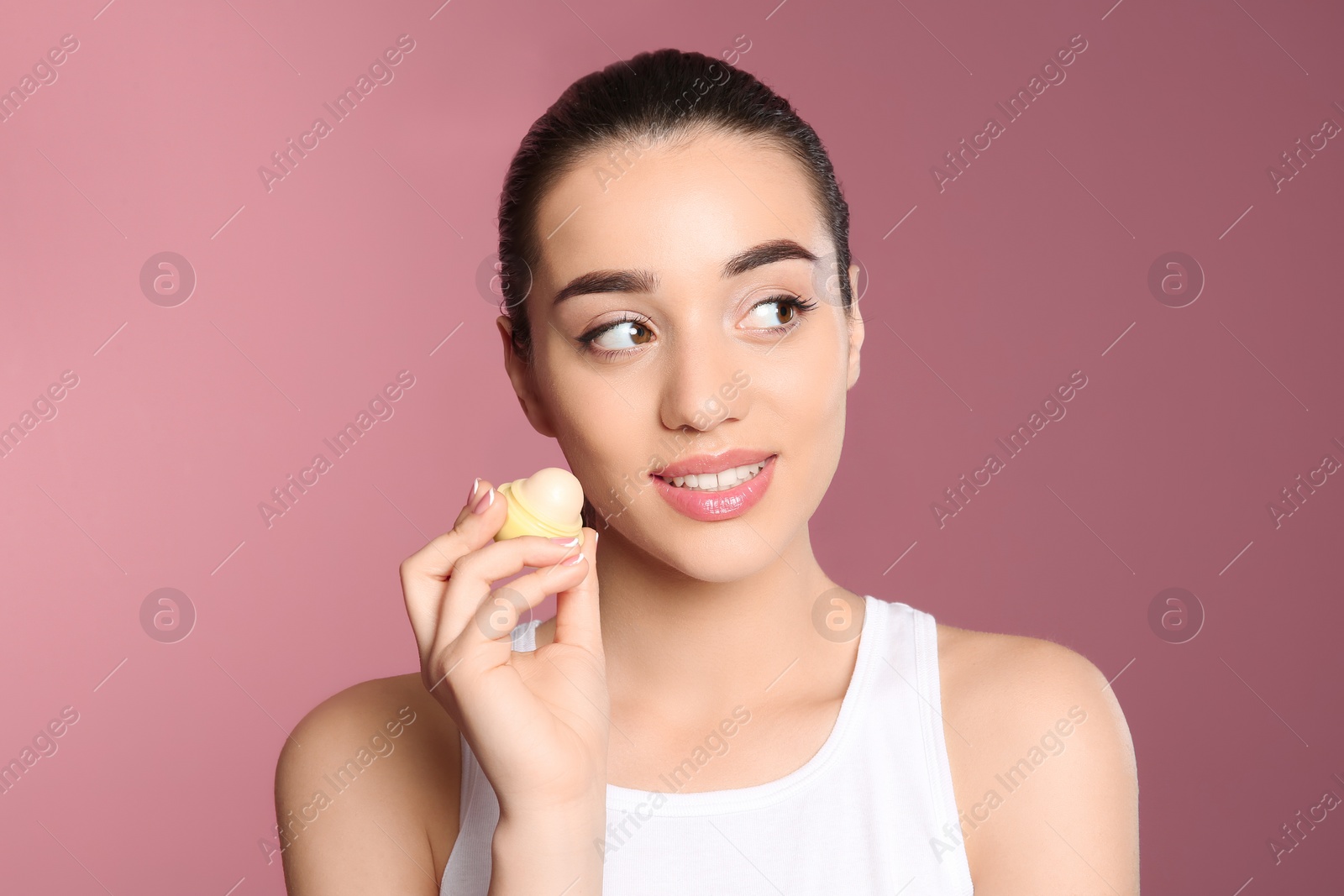 Photo of Young woman applying balm on her lips against color background