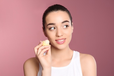 Young woman applying balm on her lips against color background