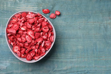 Photo of Bowl and dried strawberries on light blue wooden table, flat lay. Space for text