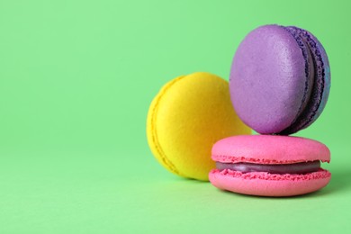 Photo of Delicious colorful macarons on green background, closeup. Space for text