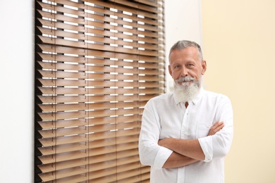 Photo of Portrait of handsome mature man near window with blinds