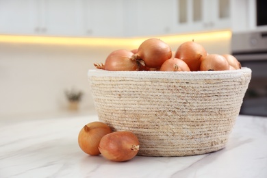 Photo of Basket with fresh onions on white marble table in modern kitchen, closeup