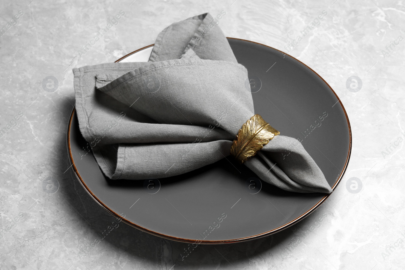 Photo of Plate with fabric napkin and decorative ring on gray marble table