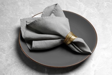 Photo of Plate with fabric napkin and decorative ring on gray marble table