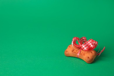 Photo of Bone shaped dog cookie with red bow on green background. Space for text