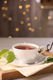 Photo of Aromatic tea in cup, saucer, spoon and green leaves on table