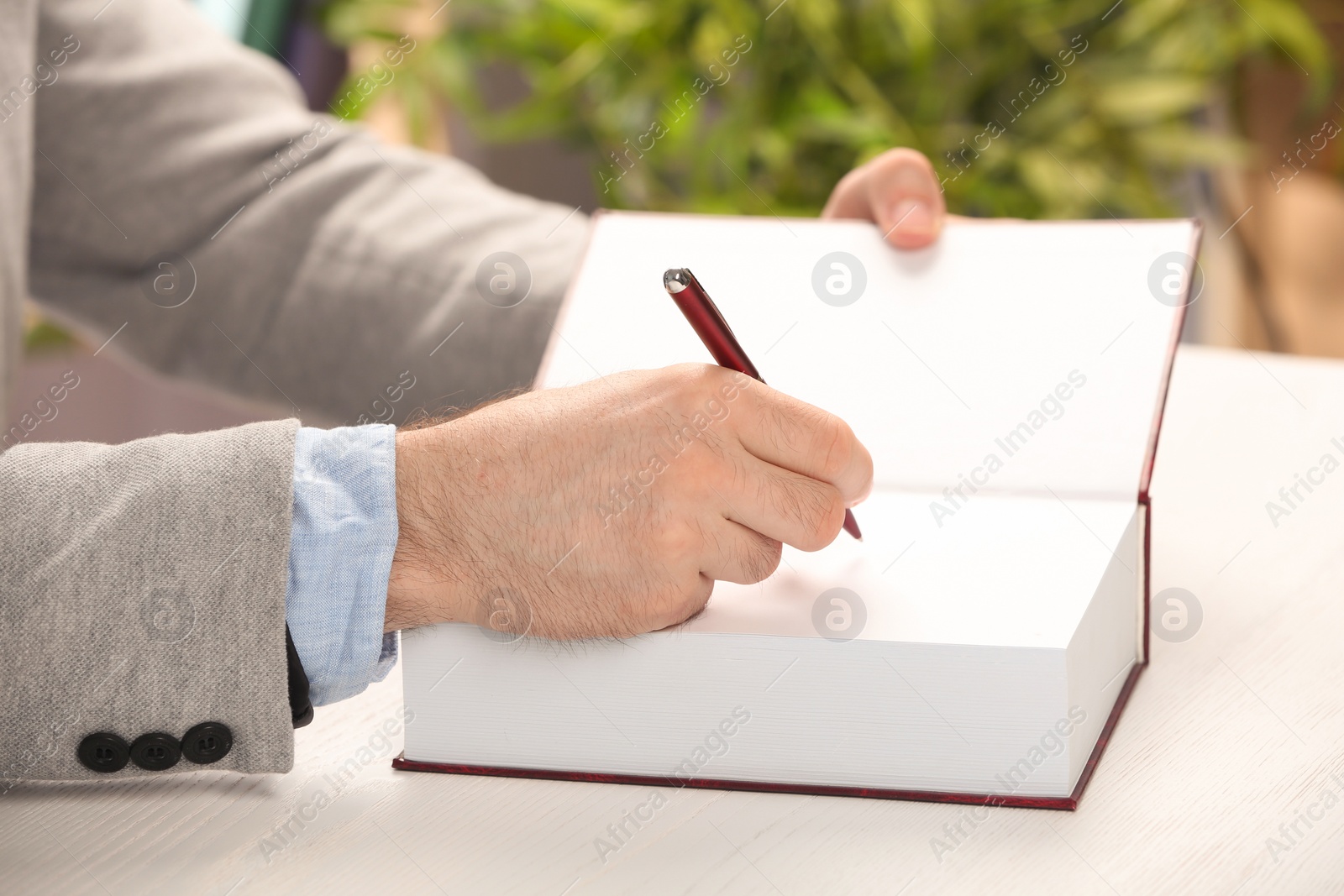 Photo of Writer signing autograph in book at table, closeup