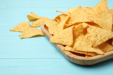 Photo of Wooden plate of tasty Mexican nachos chips on light blue wooden background