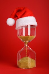 Photo of Hourglass and Santa hat on red background. Christmas countdown